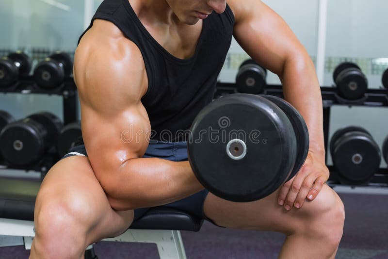 行使与在健身房的哑铃的一个年轻肌肉人的中间部分 照片拍摄时间
