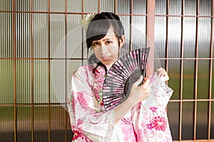 Asian woman wearing a kimono in front of Japanese wooden windows