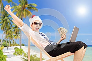 Excited man with santa hat on a beach chair holding banknotes