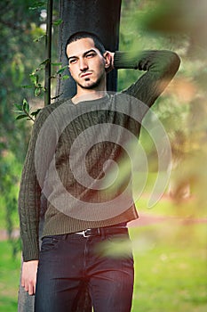 Model man short hair leaning against a tree in a nature scene