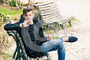 Young man sitting on the bench thinking waiting with phone in hand