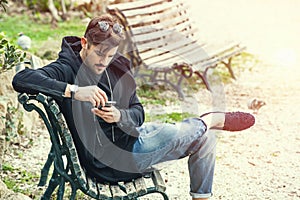Young man sitting on the bench waiting with phone in hand