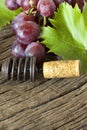 Corkscrew with cork old a between red grapes and vine leaves on rustic wooden background Royalty Free Stock Images
