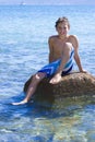 Eleven years old boy sitting on a rock in the sea