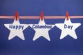 Happy Columbus Day message greeting written across white star cards hanging from red stripes ribbon and pegs on a line