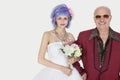 Portrait of happy senior man standing arm in arm with beautiful daughter in wedding dress against gray background