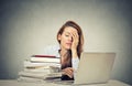 Tired sleepy young woman sitting at her desk with books in front of computer