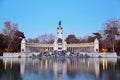 Tourists sit near monument to Alfonso XII at pond in Retiro Park