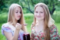 Two young happy young women eating strawberry jam on summer green outdoors background