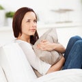 Woman daydreaming at home sitting in an armchair hugging a cushion and staring into space Stock Photos
