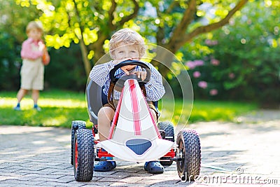 Active little boy driving pedal car in summer garden