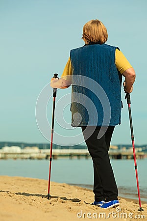 Active woman senior nordic walking on a beach. from behind