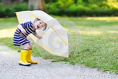 Adorable little child in yellow rain boots and umbrella in summe