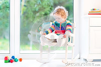  book in a white rocking chair next to a big window with garden view