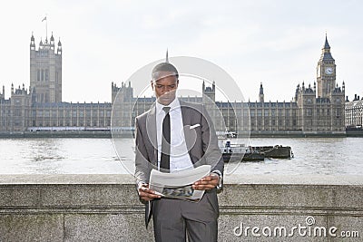 African American businessman reading newspaper with building in background