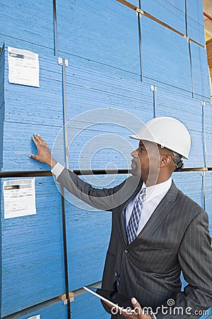 African American male contractor inspecting wooden planks while holding tablet PC