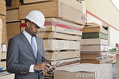 African American male contractor using tablet PC with stacked wooden planks in background