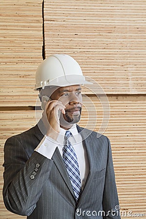 African American male engineer on phone call with stacked wooden planks in background