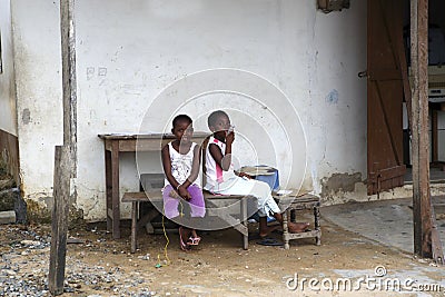 African girls sit in front of a house