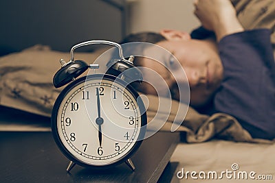 Alarm clock with male model in bed in background.