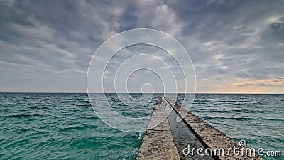 Alone concrete pier with clear ocean and stormy clouds