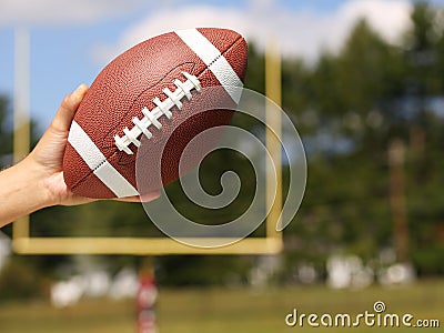 American Football in Hand over Field with Goal Post