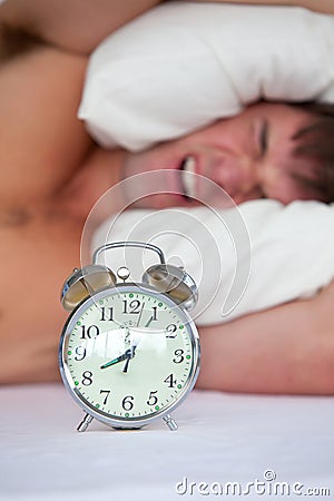 Angry man in bed annoyed by his alarm clock