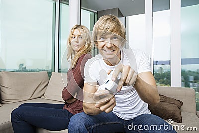 Angry woman looking at man play video game in living room at home