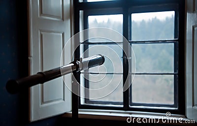 An antique telescope in front of window.