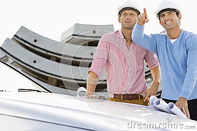 Architects with blueprints on car discussing at construction site
