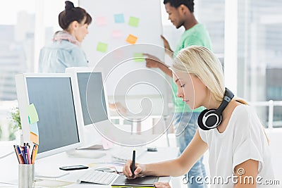 Artist drawing something on graphic tablet with colleagues behind at office