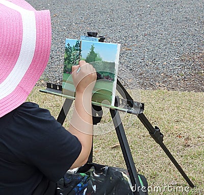 Artist lady sitting and painting on canvas outside.