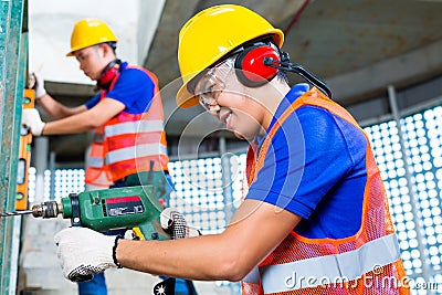 Asian construction workers drilling in building walls