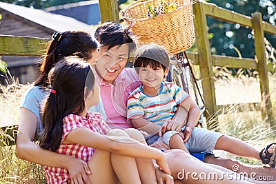 Asian Family Resting By Fence With Old Fashioned Cycle