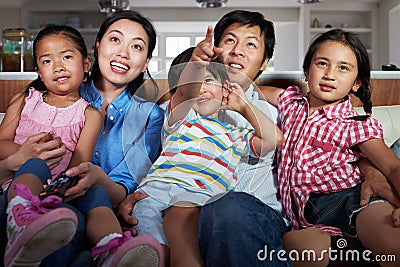 Asian Family Sitting On Sofa Watching TV Together