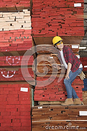 Asian female industrial worker standing on stacked wooden planks holding tablet PC