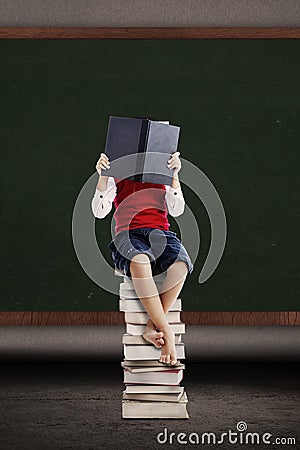 Asian kid reading a book on stack of books