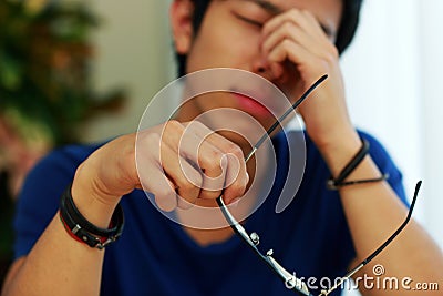 Asian man with eye pain holding glasses