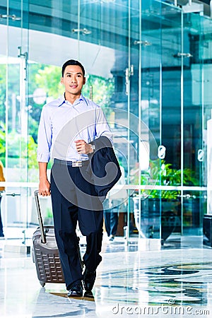 Asian man pulling suitcase in hotel lobby