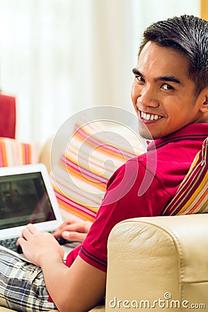 Asian man sitting on couch surfing the internet