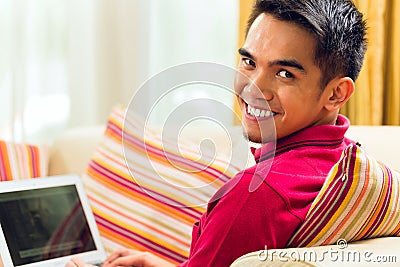 Asian man sitting on couch surfing the internet