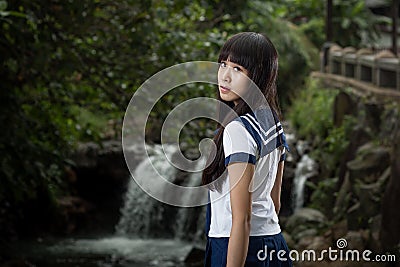 Asian schoolgirl standing in front of waterfall