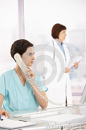Assistant taking phone call, doctor in background