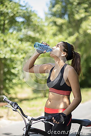 Athletic woman drinking water after exercise with bicycle