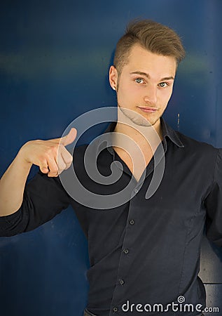 Attractive blond, blue eyed young man smiling and doing thumb up sign