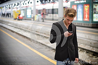 Attractive blond young man in station using cellphone