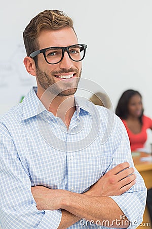 Attractive designer smiling at camera with colleagues behind him