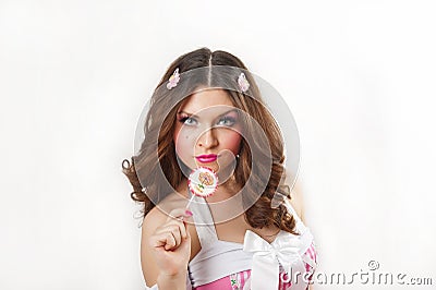 Attractive girl with a lollipop in her hand and pink dress isolated on white. Beautiful long hair brunette playing with a lollipop