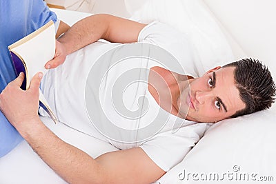 Attractive man in pajamas lying on the bed reading book