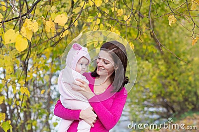 Attractive mother holding a baby girl playing with falling autumn leaves